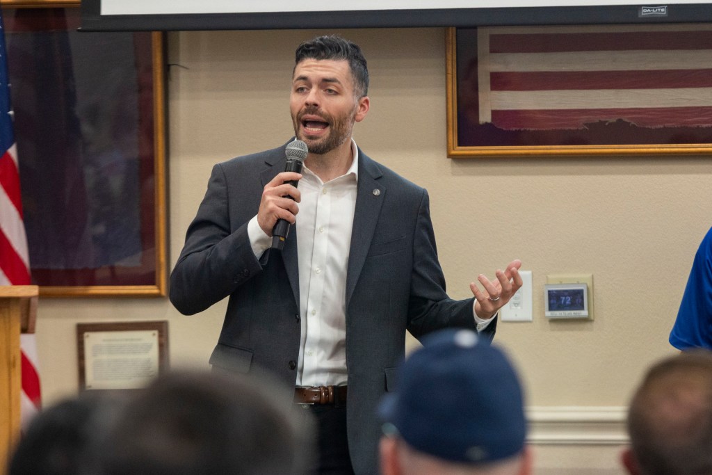 A man in a suit holding a microphone in a meeting room.