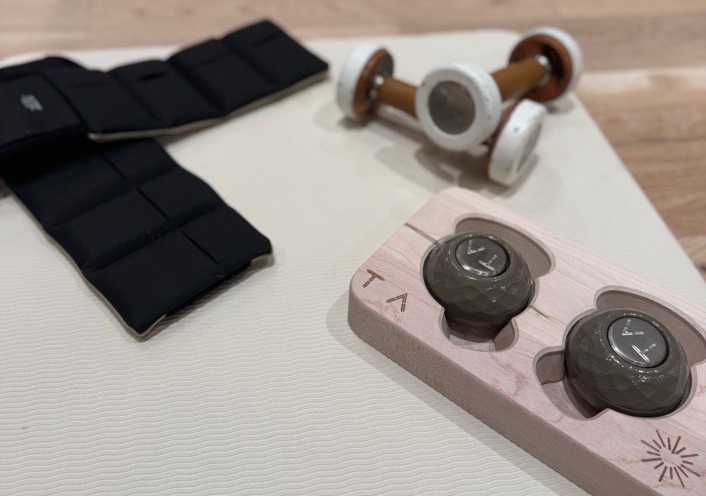 photo of a yoga mat with exercise on it, including dumbbells and circular weights inside a wooden compartment