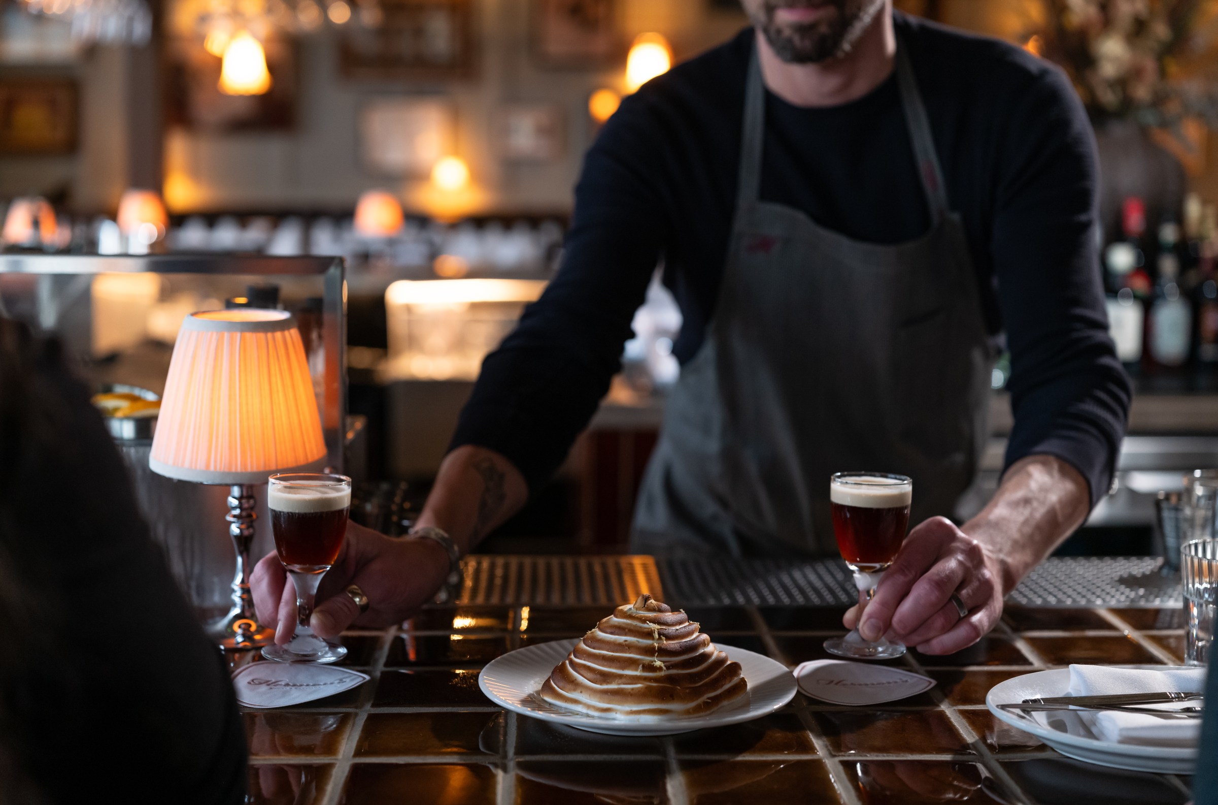 Baked alaska on a tiled bar with a man standing behind it at Hermon’s