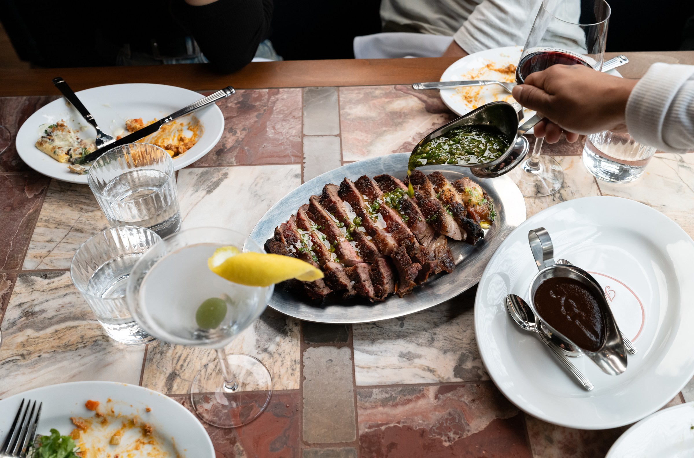 Hand drizzling sauce from a silver saucer onto an awaiting rib-eye at Hermon’s
