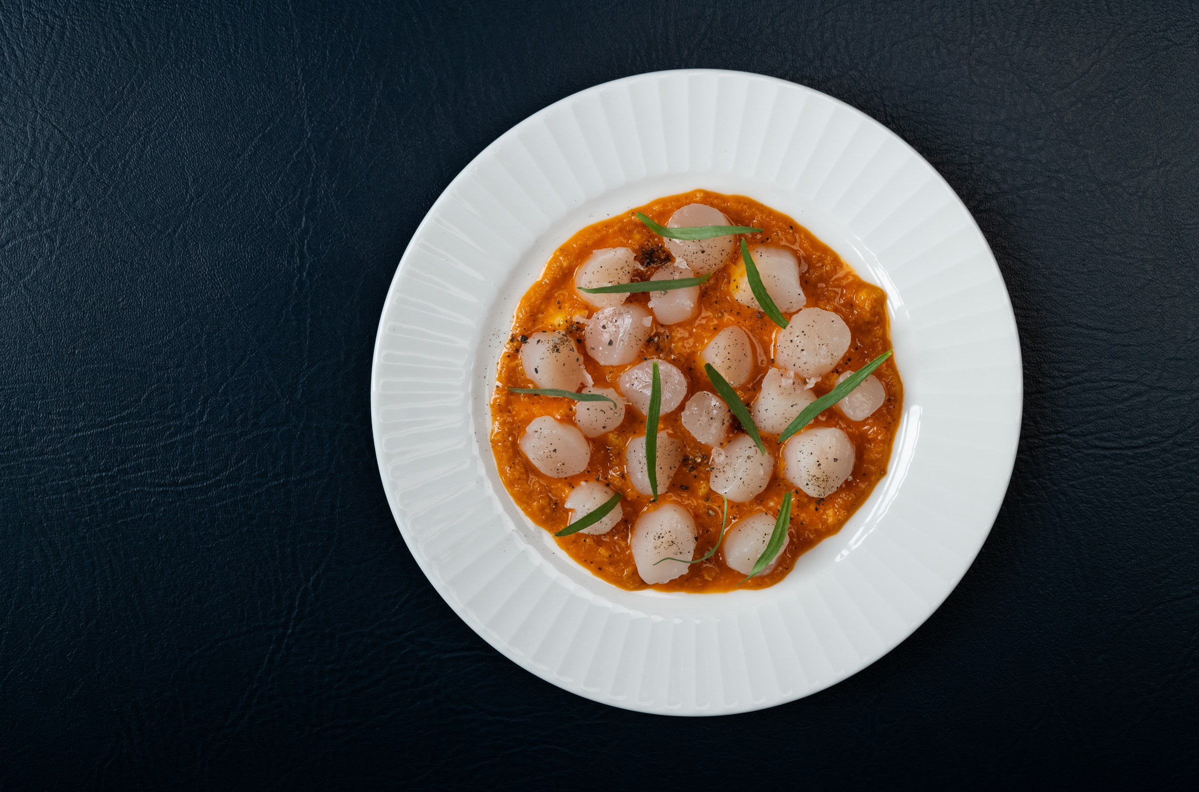 Scallop crudo photographed from above on sun-dried tomato sauce at Hermon’s