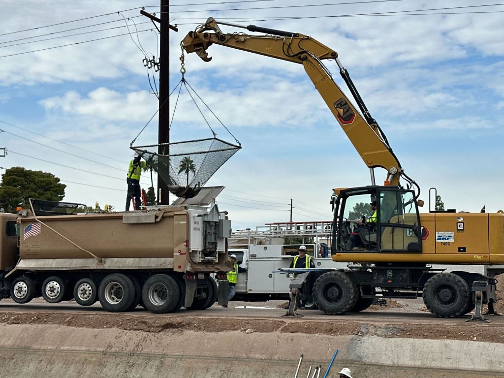A massive excavator construction vehicle lifts a giant net filled with Amur fish and lowers it into a waiting truck.