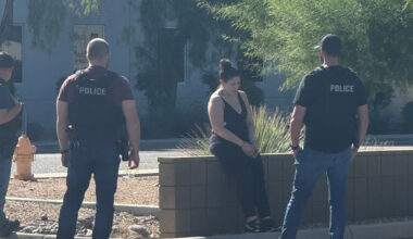 police surround a woman sitting on a low block wall