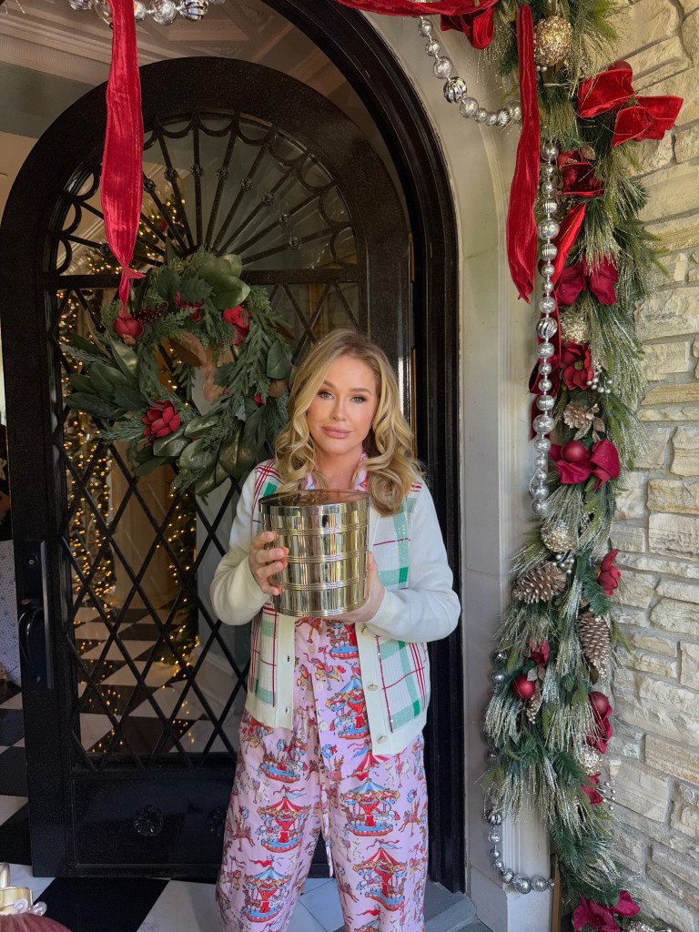 Kathy Hilton holding a Slatkin Co. gift set in front of a holiday-decorated doorway.