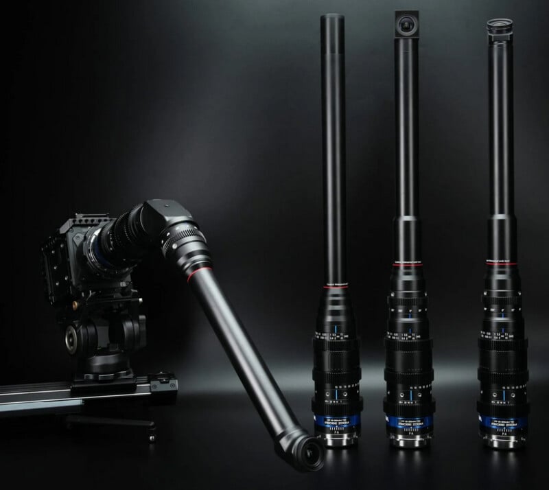 A set of four long, black periscope-style camera lenses are displayed on a dark surface; one lens is attached to a camera mounted on a tripod, and three stand upright beside it.
