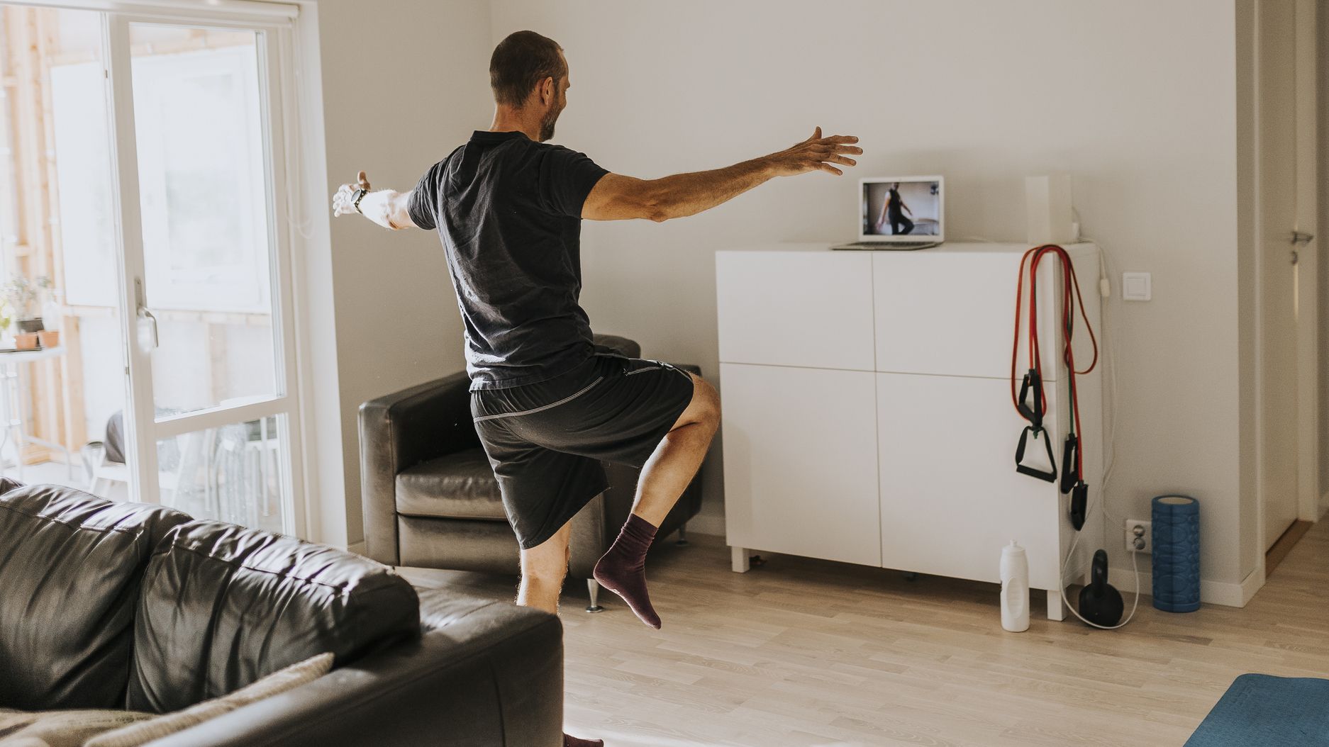 Man stands on one leg in living room in front of laptop