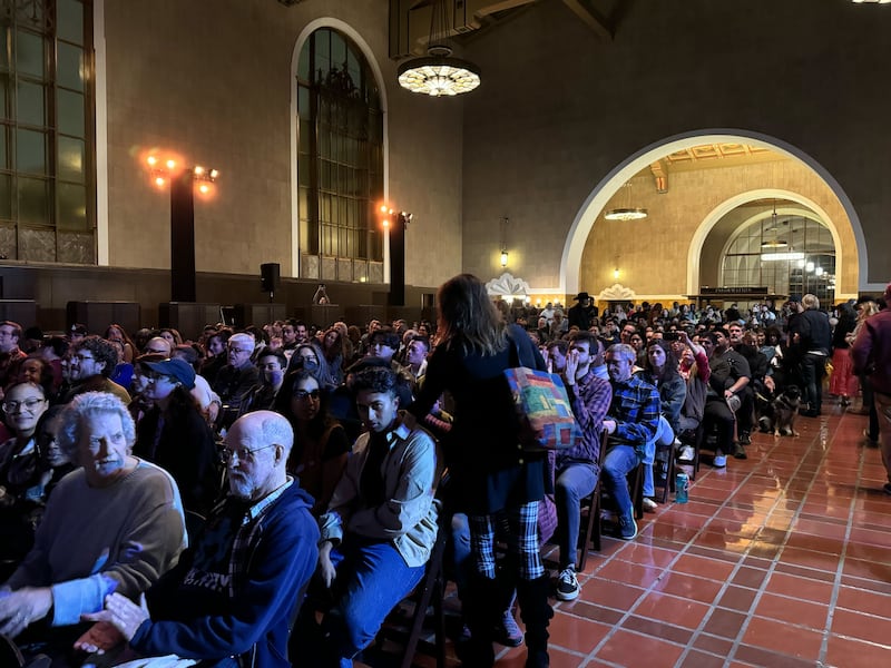 A crowd of people wait inside Union Station, which is set like like an auditorium. It is evening and people are finding their seats.