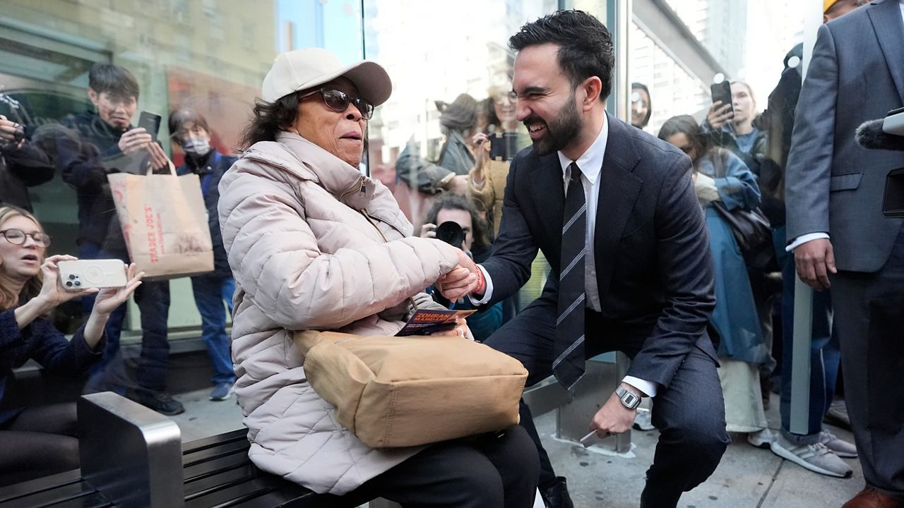 Then-mayoral candidate Zohran Mamdani speaks with a bus rider as she waits at a stop in the city on Monday, Oct. 27, 2025. (AP Photo/Seth Wenig)