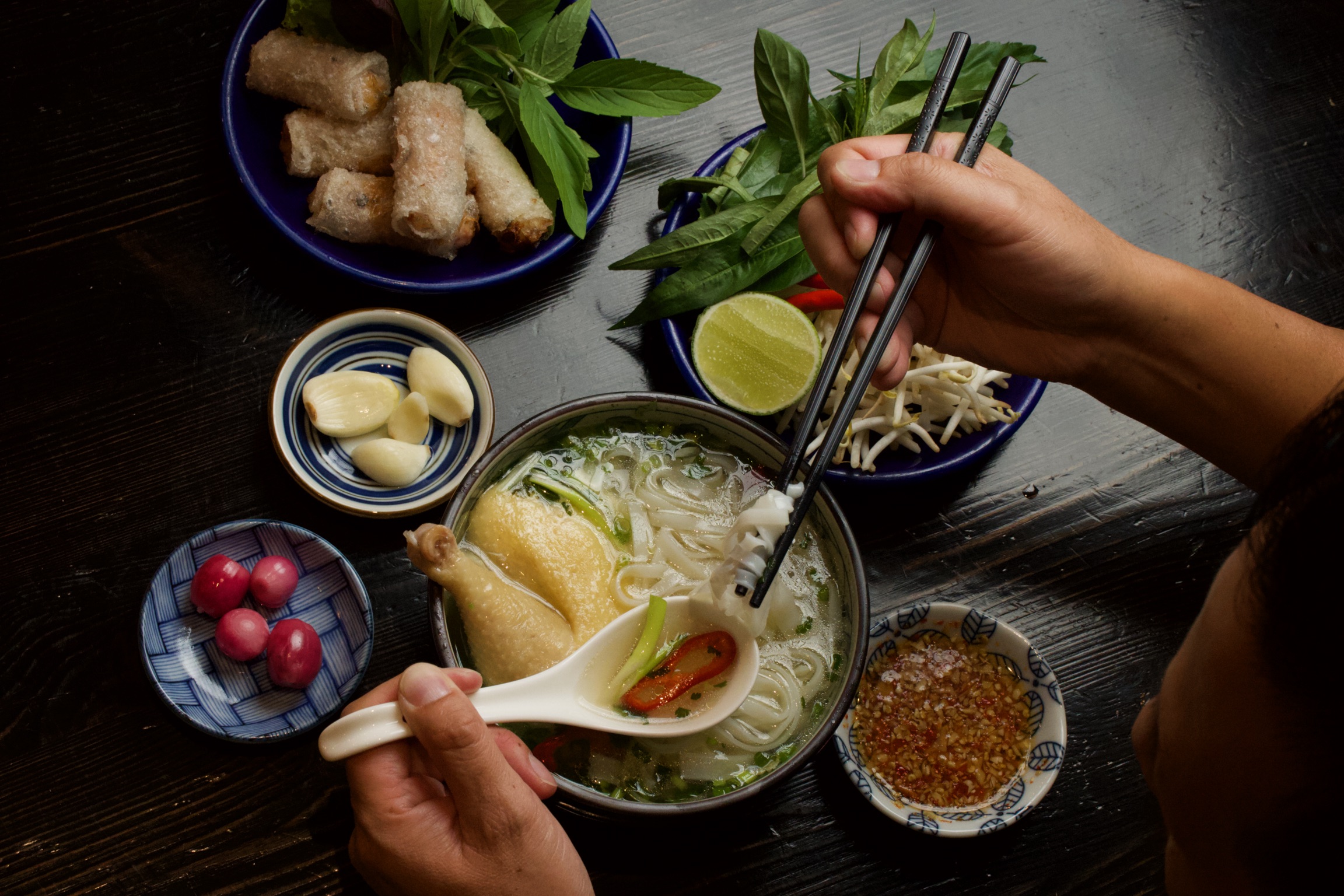 Overhead shot of hands dipping into pho bowl at Pho Go Gao.