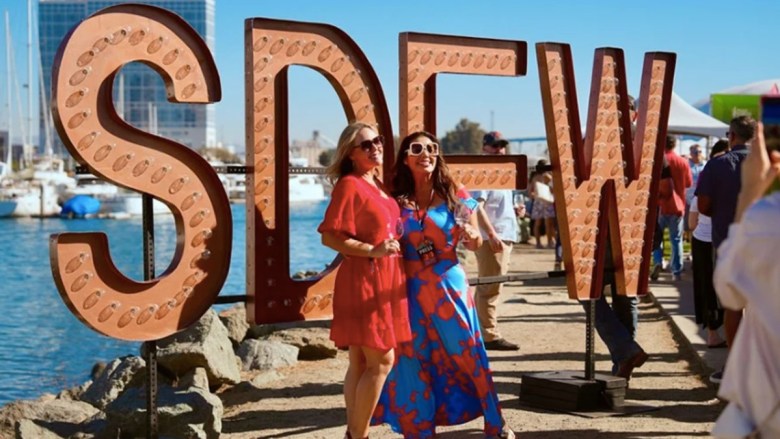 Two women posing in front of large marquee letters spelling "SDFW" at a waterfront event.