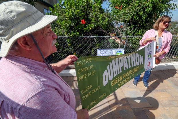 Talmage residents Michael Pound and Sarah Axford, who are the co-founders of the Talmage Fire Safe Council, unfurl a banner they had made while in Pound's backyard in San Diego on Friday, Oct. 31, 2025. (Hayne Palmour IV / For The San Diego Union-Tribune)
