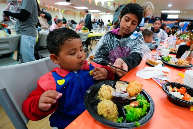 At the annual Thanksgiving Dinner hosted by the San Diego Rescue Mission, Rhianna Puentes helps with feeding her younger brother, Nathaniel. The Puentes children, along with their mother, are currently living out of their car.  (Nelvin C. Cepeda / The San Diego Union-Tribune)