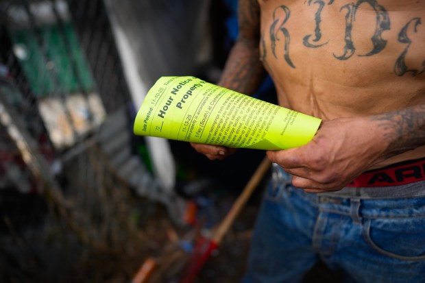 Andrew Shields, 56, holds out the 72-hour notice that was posted to his makeshift shelter at his encampment near the I-5 freeway on Tuesday.  Shields recently asked officers from the San Diego Police Department for shelter but was told there was no room. (Nelvin C. Cepeda / The San Diego Union-Tribune)