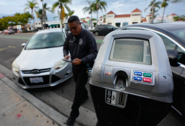 A San Diego parking enforcement officers issues a ticket for an expired meter on University Avenue in Hillcrest on Thursday, Nov. 20, 2025. San Diego is moving forward with its plan to eliminate free Sunday parking by creating a paid permit program for people living within two blocks of paid parking zones. They will be able to park at a meter on Sundays all day without paying anything. (Nelvin C. Cepeda / The San Diego Union-Tribune)