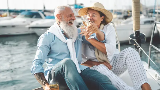 Senior couple toasting champagne on sailboat vacation - Happy elderly people having fun celebrating wedding anniversary on boat trip - Love relationship and travel lifestyle concept.