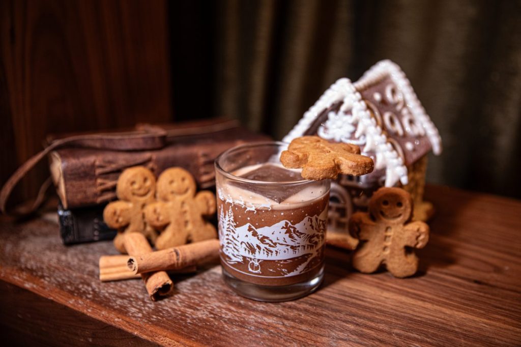 A holiday cocktail with gingerbread men cookies and a gingerbread house.