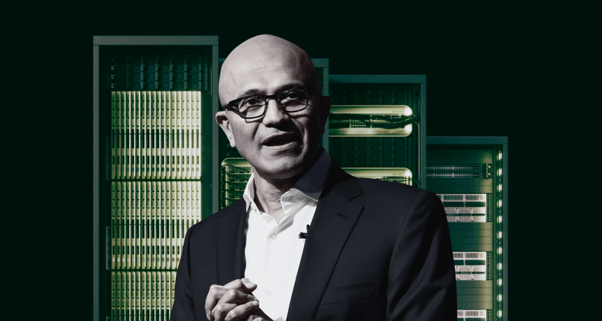 Man in a suit stands in front of a row of server racks.