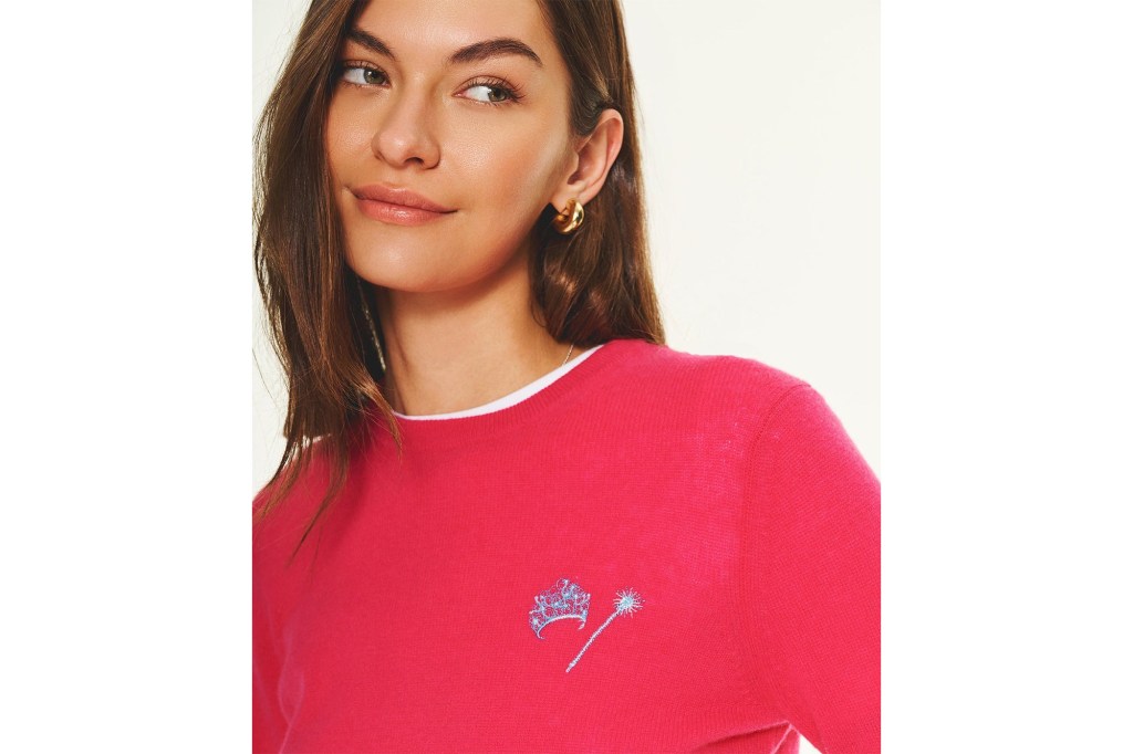 Woman wearing a hot pink sweater with an embroidered tiara and magic wand.