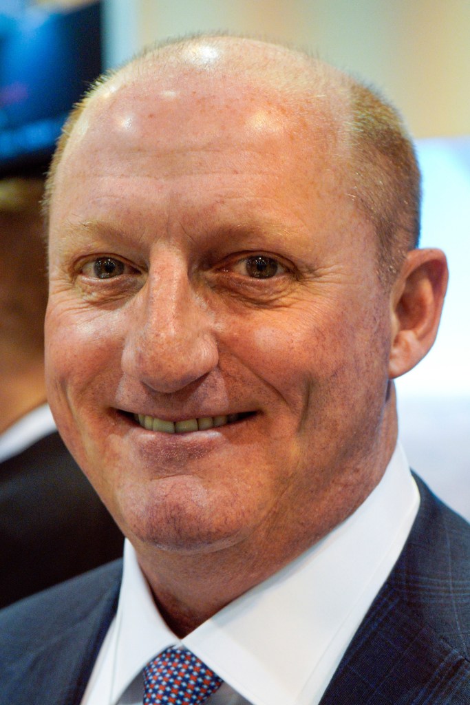 Berkshire Hathaway Vice Chairman Greg Abel smiles in a dark suit and a white shirt with a patterned tie.
