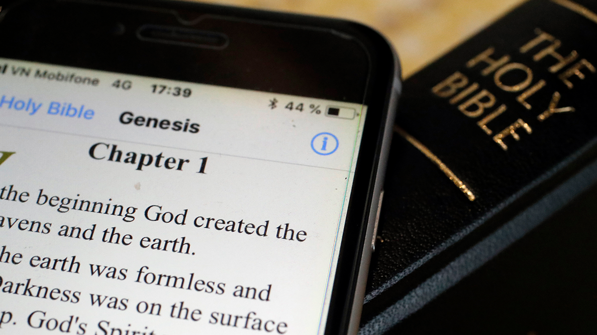 The Bible app opened on a phone next to a print Bible