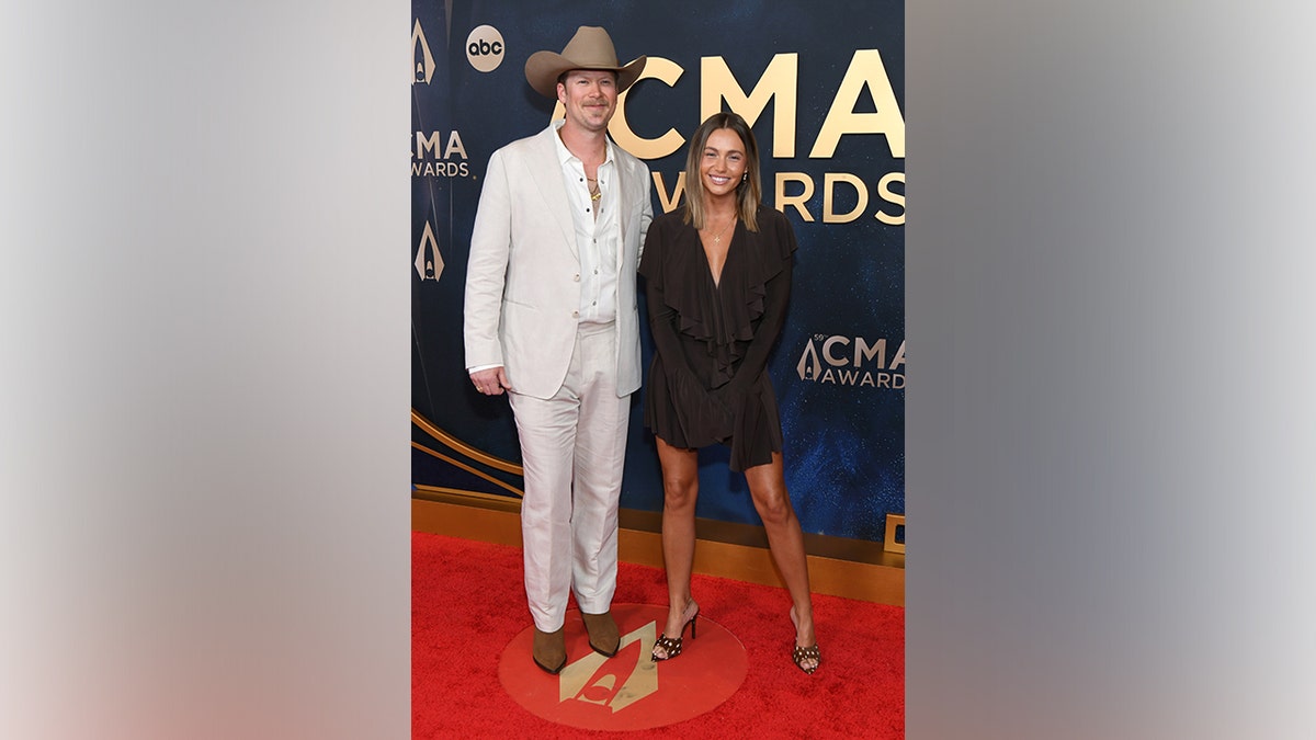 Brian Kelley, wearing a light beige suit, white shirt, and cowboy hat, poses on the red carpet with Brittney Marie Kelley, dressed in a dark brown ruffled mini dress and heels, at the 59th Annual CMA Awards in Nashville, Tennessee, on November 19, 2025.
