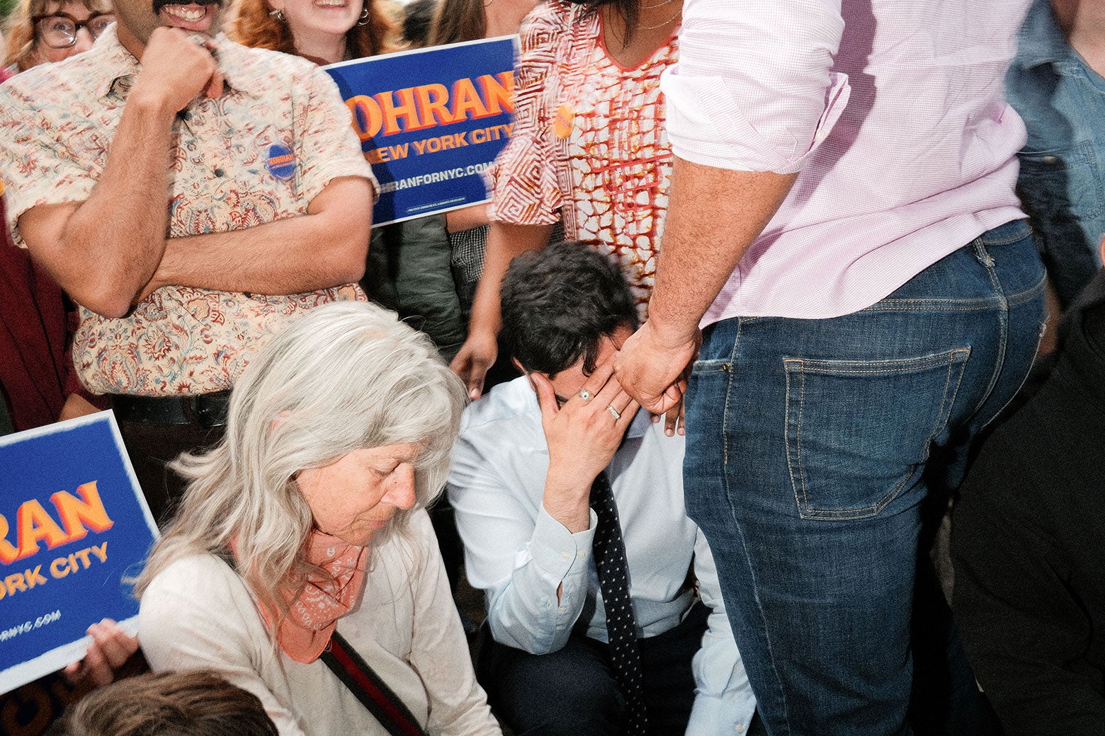 Mamdani kneels and covers his face while surrounded by voters.