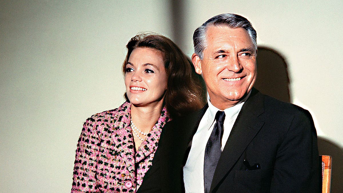 Cary Grant and a young Dyan Cannon sitting together and smiling not looking at the camera.