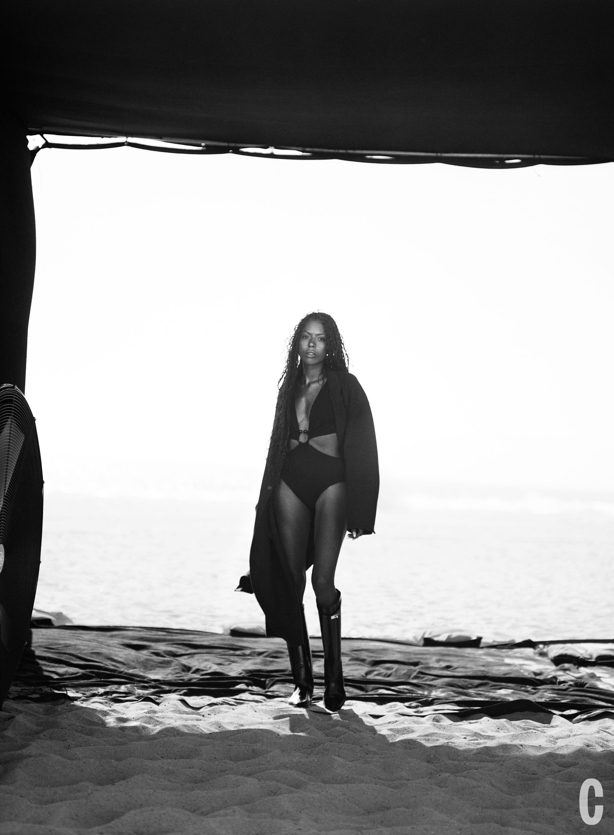 a person walks on the beach wearing a swimsuit and a long coat
