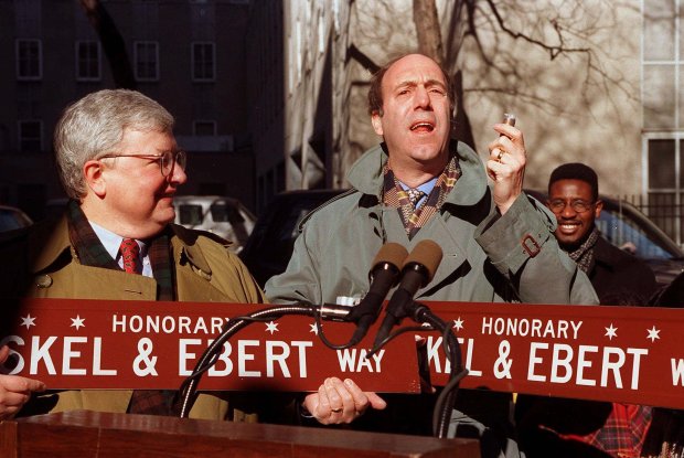 Gene Siskel, right, and Roger Ebert speak at an event where Erie Street at McClurg Court is renamed to honor the movie critics on Feb. 1, 1995. Siskel is holding a roll of quarters in which he fed the parking meters along Erie Street. (Chris Walker/Chicago Tribune)