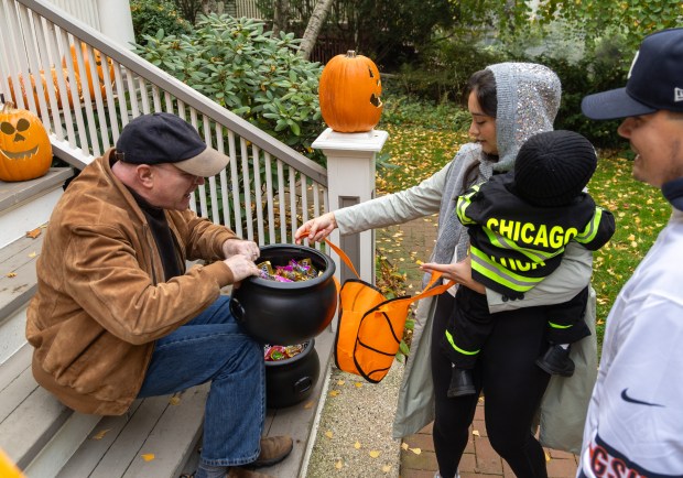 Larry Bauer, left, offers candy to Amanda Moncivais, center, as she holds her crying son Luca Vieni, 1, as his dad Mike Vieni looked on during trick-or-treating on Monroe Street in Evanston, Oct. 31, 2025. (Dominic Di Palermo/Chicago Tribune)