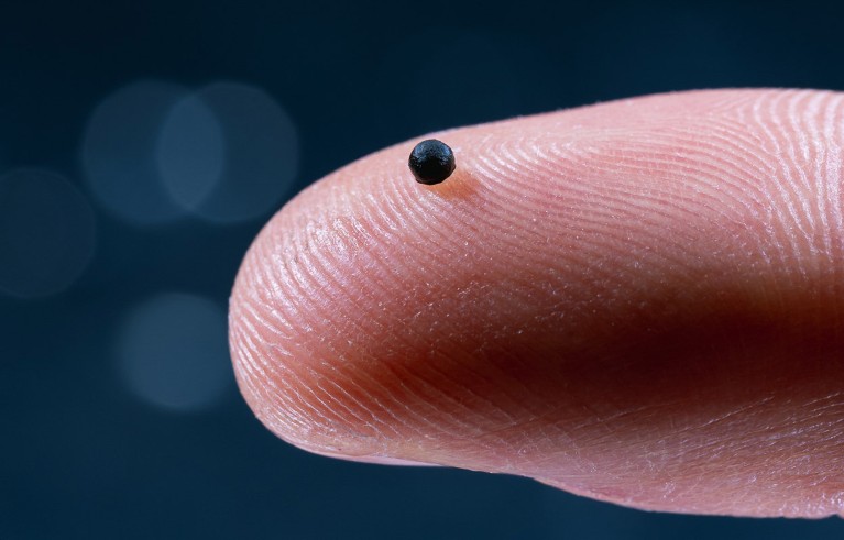 Close up of a single black sphere ETH micro robot displayed on a person's finger tip.