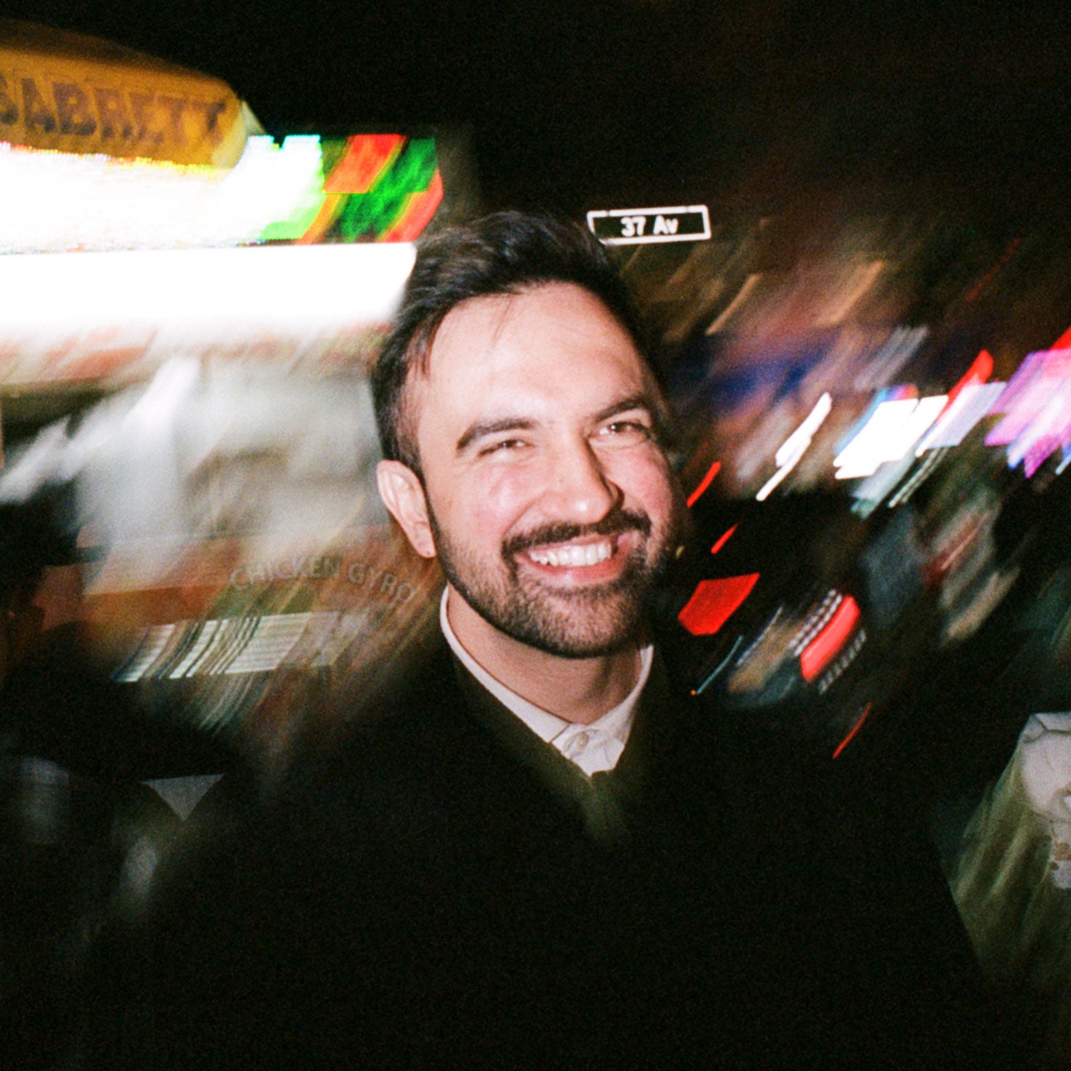 Mamdani smiles in front of a blurred image of vibrant New York.