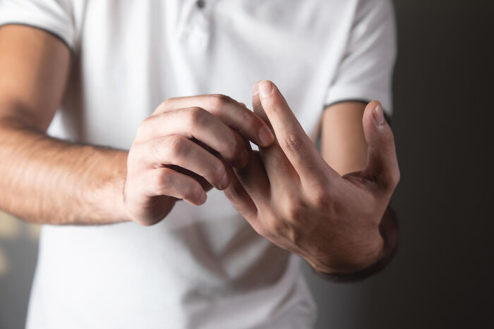 Person in white shirt examining finger pain, illustrating Dr. Google versus real doctor medical advice conflict.