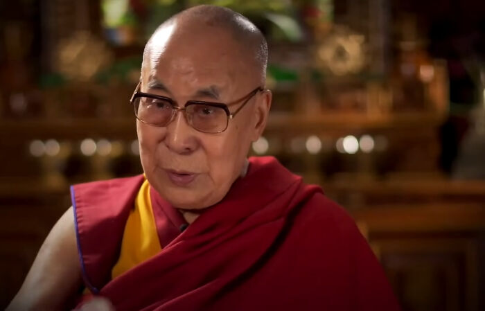 Elderly man in glasses wearing traditional robe, speaking in a warmly lit room about Dr. Google and real doctor debates.