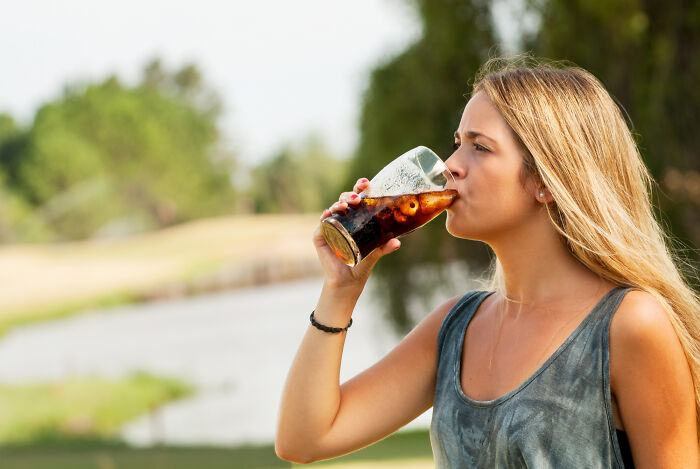 Young woman drinking soda outdoors, illustrating a common topic in Dr. Google versus real doctor health debates.