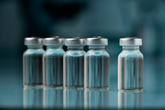 Five small clear medical vials with silver caps on a reflective surface, highlighting Dr Google versus real doctor theme.