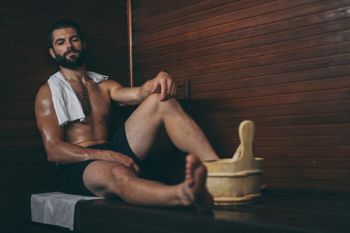 Bearded man relaxing in a wooden sauna, towel over shoulder, illustrating contrast between Dr Google advice and real doctor care.