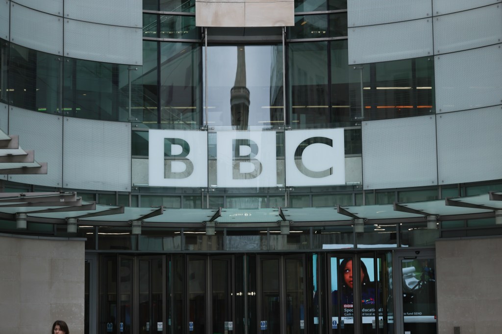 Exterior of the BBC building with "BBC" branding and a reflection of a spire in the glass facade.
