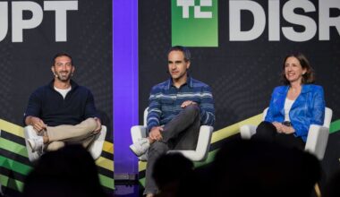 Three speakers talk on a stage with a black backdrop.