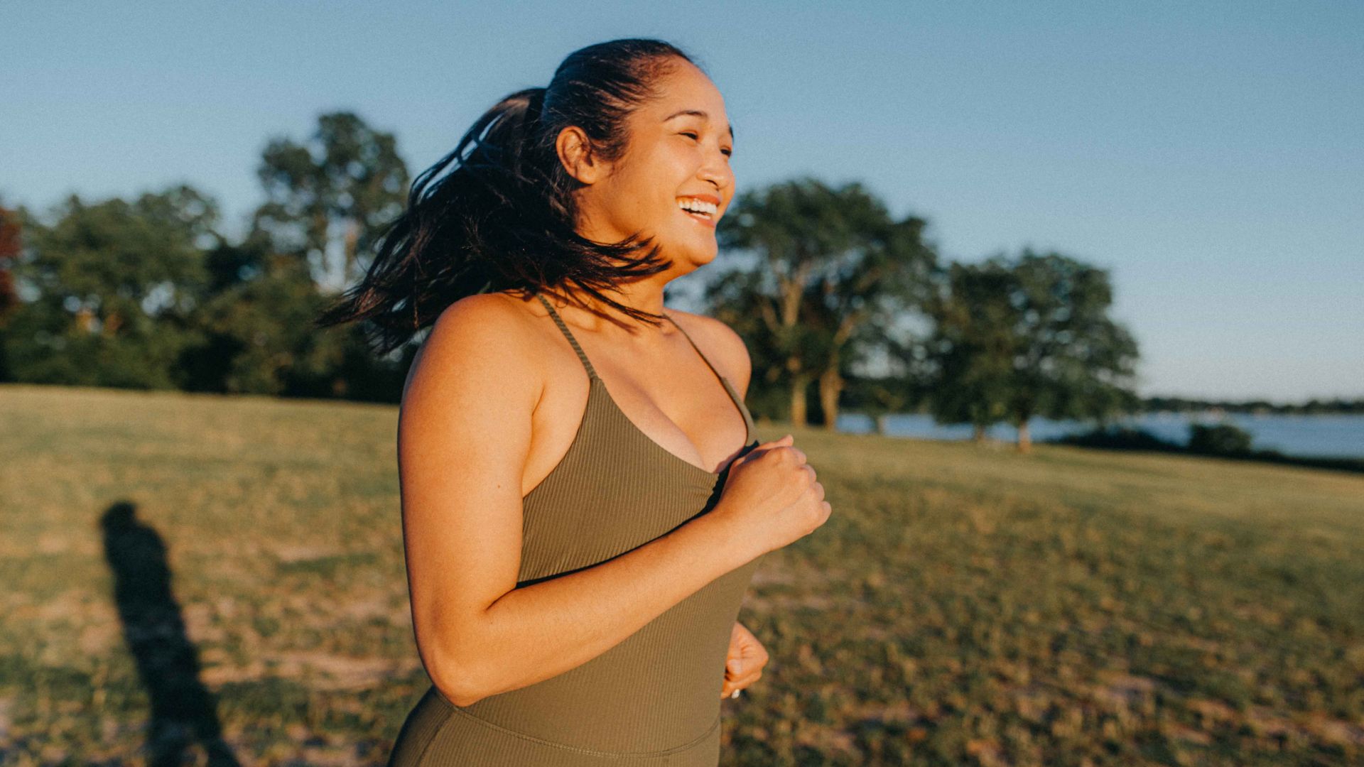 A smiling woman runs outside in a field in the afternoon sun.