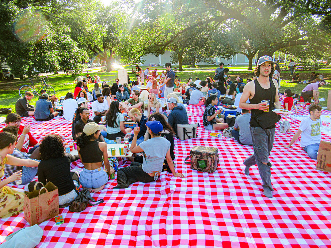 Photo of a crowd of people sitting on a red-and-white checkered picnic blanket.