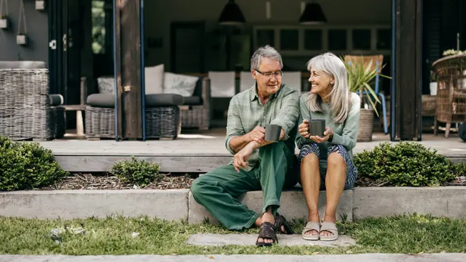 With coffee in hand, a senior couple in their 60s embraces a quiet moment, appreciating the beauty of their home.