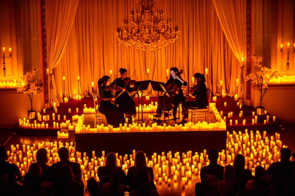 A string quartet performing on a raised stage amid a sea of candles as the silhouette of audience members watches
