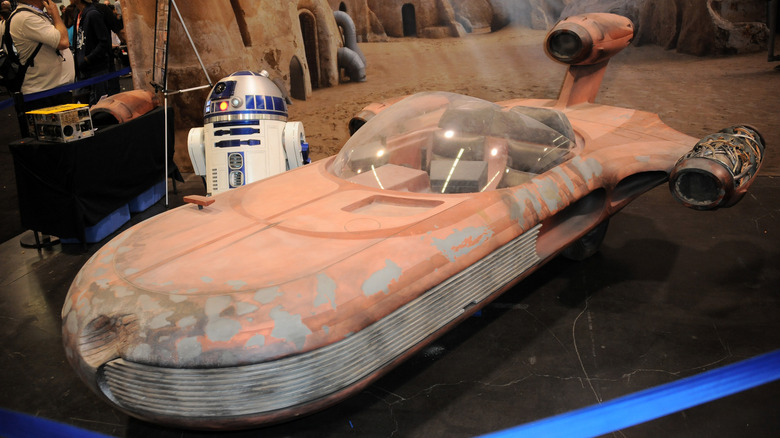 R2D2 next to a :andspeeder at a Star Wars convention.
