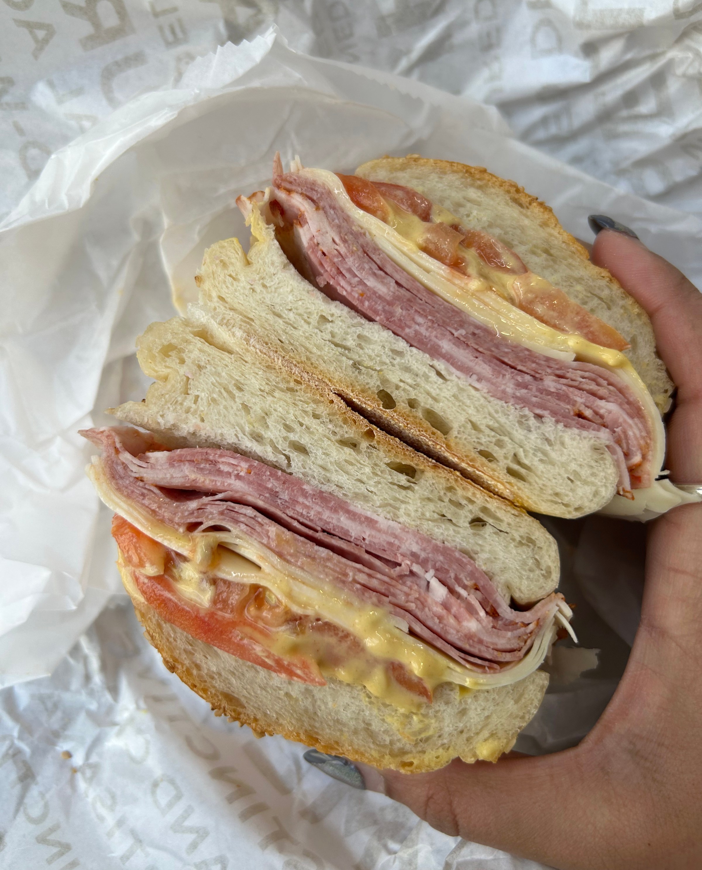 Two halves of a sandwich with meat, tomatoes, and mustard being held up.