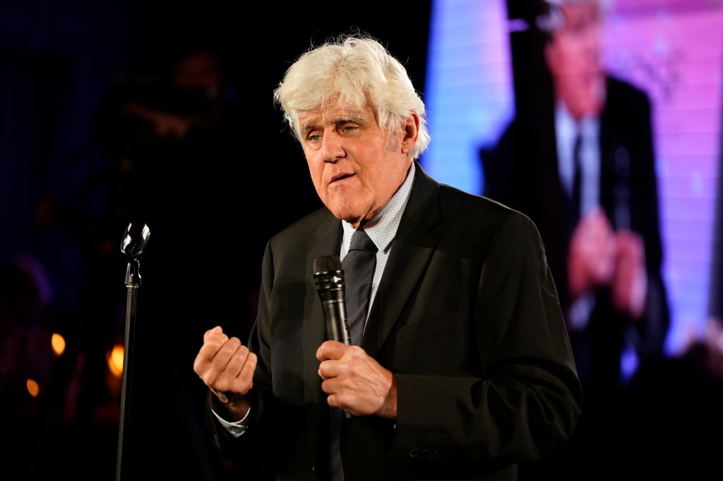 Jay Leno speaks onstage, holding a microphone.