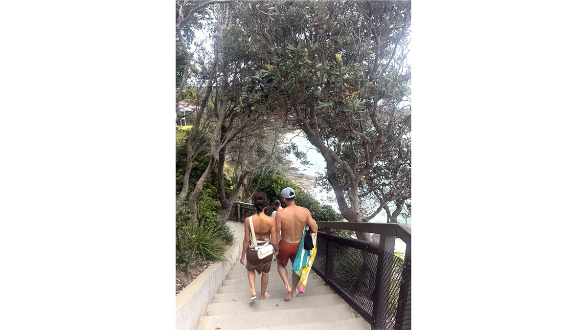 Jessica Alba and Danny Ramirez walk hand in hand down a staircase toward the beach in Australia.