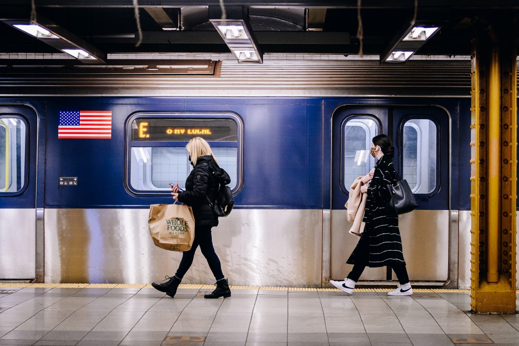 People wearing protective masks walk past a subway train.