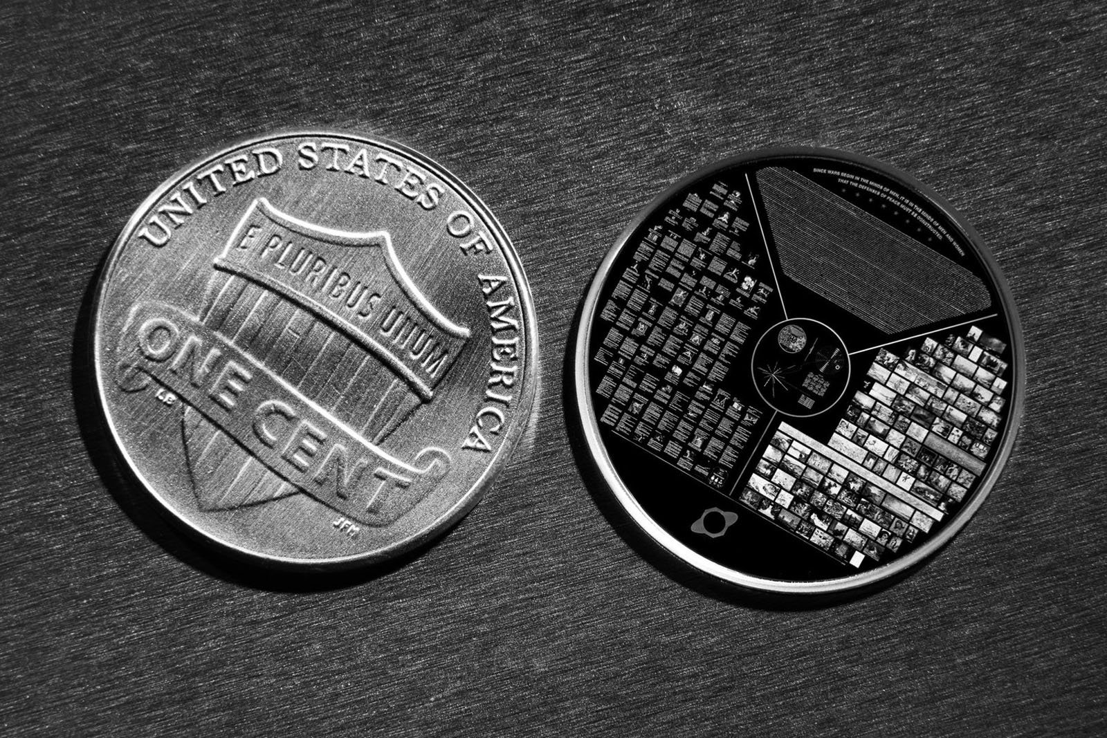 A close-up of a U.S. one cent coin next to a circular object with intricate, grid-like patterns, both placed on a dark, textured surface.