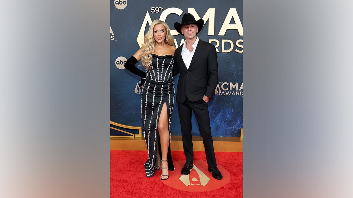 Megan Moroney, wearing a black strapless gown with pearl details and thigh-high slit, poses on the red carpet alongside Kenny Chesney, dressed in a black suit, white shirt, and black cowboy hat, at the 59th Annual CMA Awards in Nashville, Tennessee, on November 19, 2025.